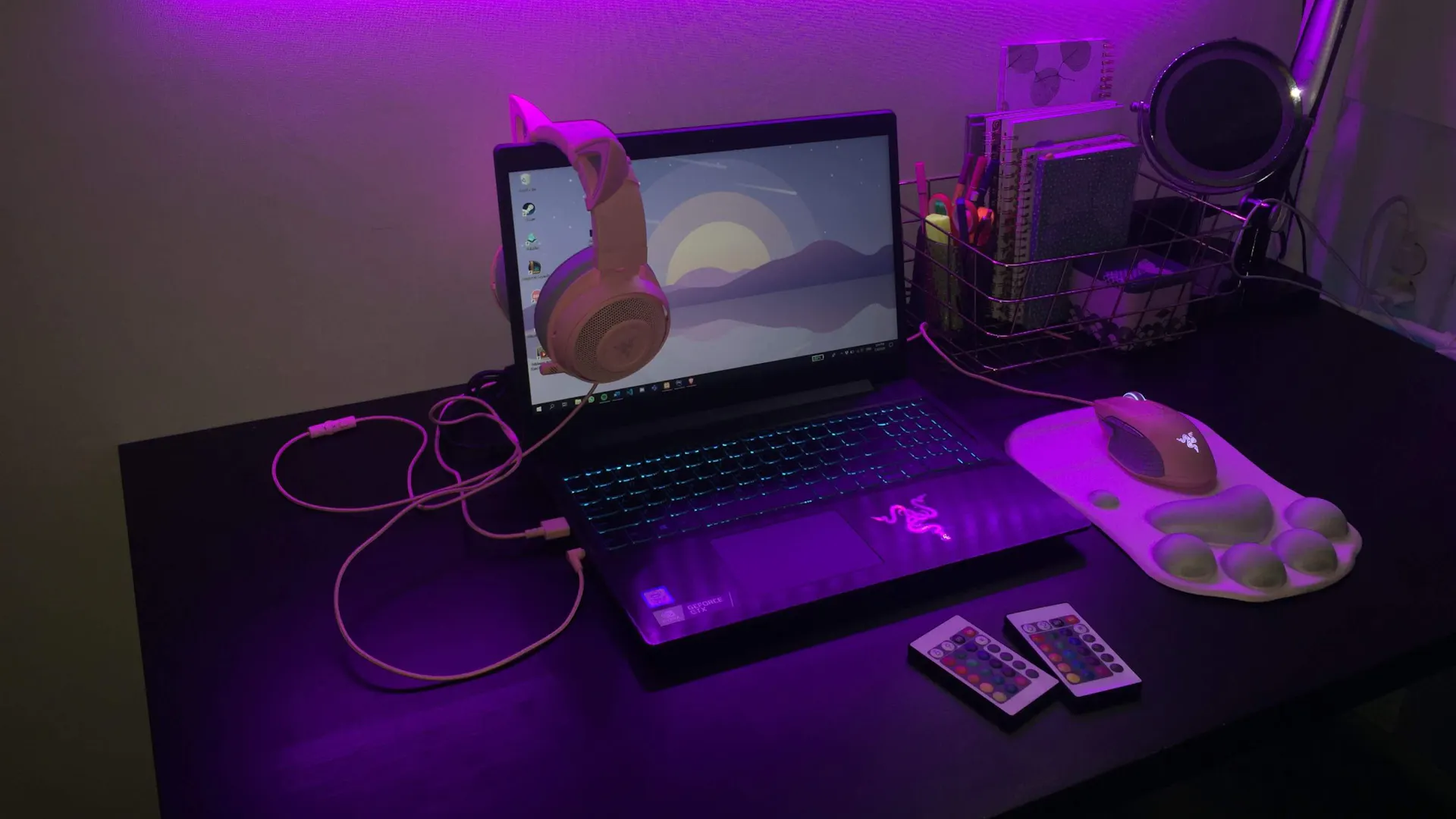 Auf einem Schreibtisch in einem lila LED beleuchteten Gaming Zimmer steht ein Gaming Laptop, Gaming Maus und einem farblich passenden Gaming Headset über dem Bildschirm