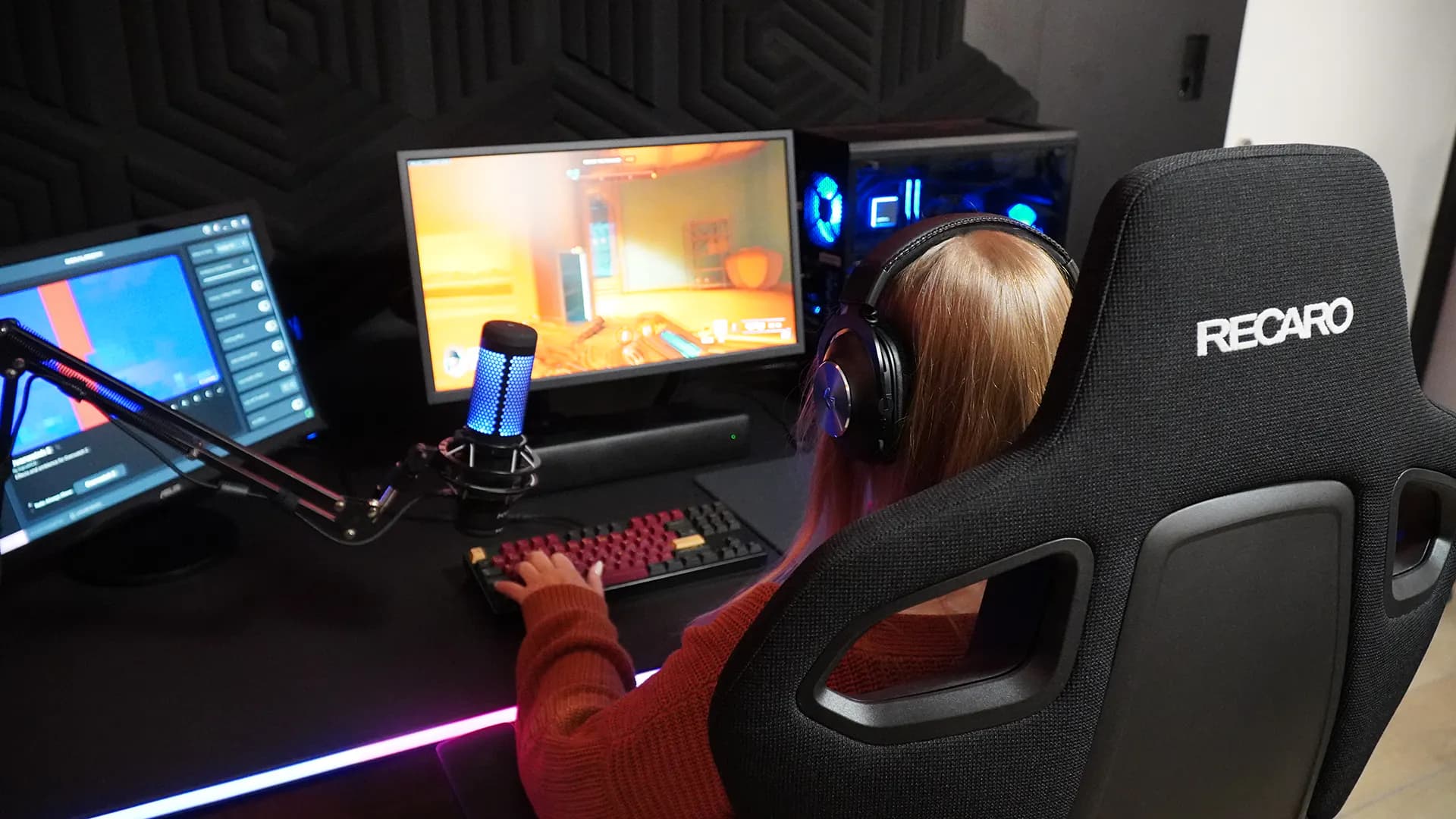 Eine Frau sitzt an einem Streaming Setup mit Mikrofon und zockt.
