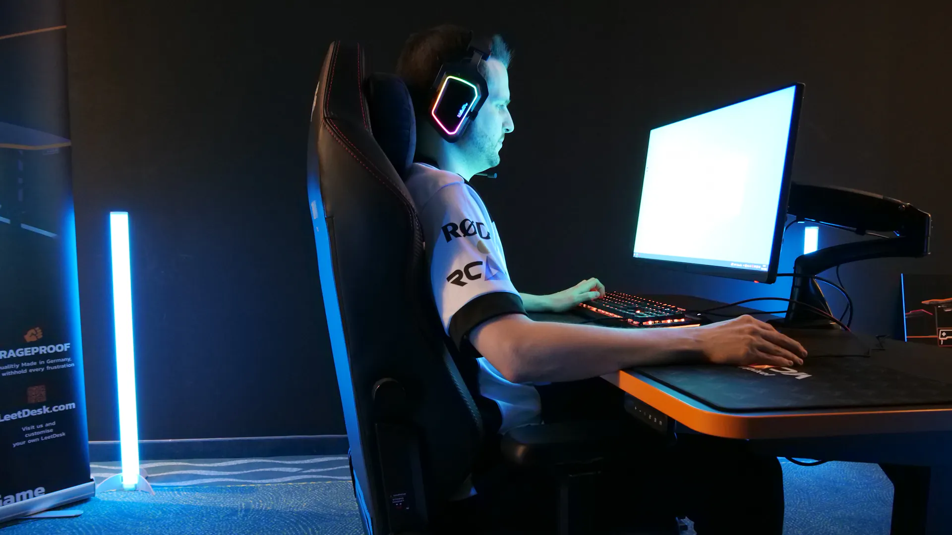 Eine Person mit LED Headset sitzt gerade, hell erleuchtet durch einen Bildschirm am LeetDesk Monitorarm, an einem Gaming Tisch von LeetDesk 