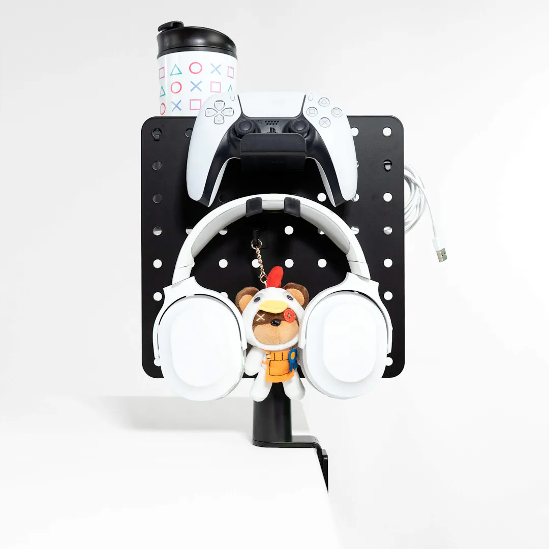 Pegboard as a gaming organiser with gaming controller, headphones, charging cable, drinking cup and a small plush toy for space-saving storage.