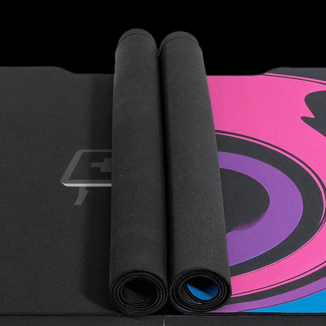 A black deskpad with a colorful swirl pattern on a height-adjustable Leetdesk, featuring dual mousepads rolled up on the tabletop. The mauspad covers a large portion of the desk surface for optimal use.